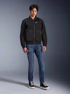 Alpinestars Flight Air Jacket, nera, giacca da moto stile bomber d'ispirazione urbana con pannelli in mesh 3D e logo bianco sul petto, indossata da un modello con jeans blu e sneakers nere, abbigliamento da moto contemporaneo