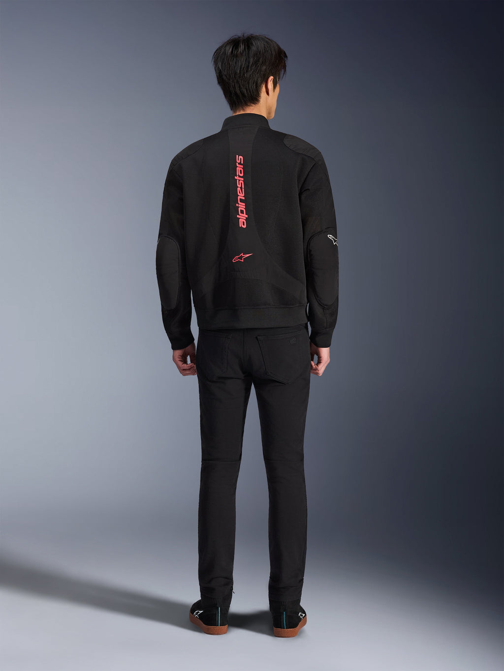Giacca Alpinestars Flight Air in Nero Rosso Brillante, vista posteriore di giacca da moto in stile bomber urbano, con branding Alpinestars verticale rosso e logo sulla schiena, costruzione leggera in mesh 3D, indossata con pantaloni neri per un look contemporaneo.