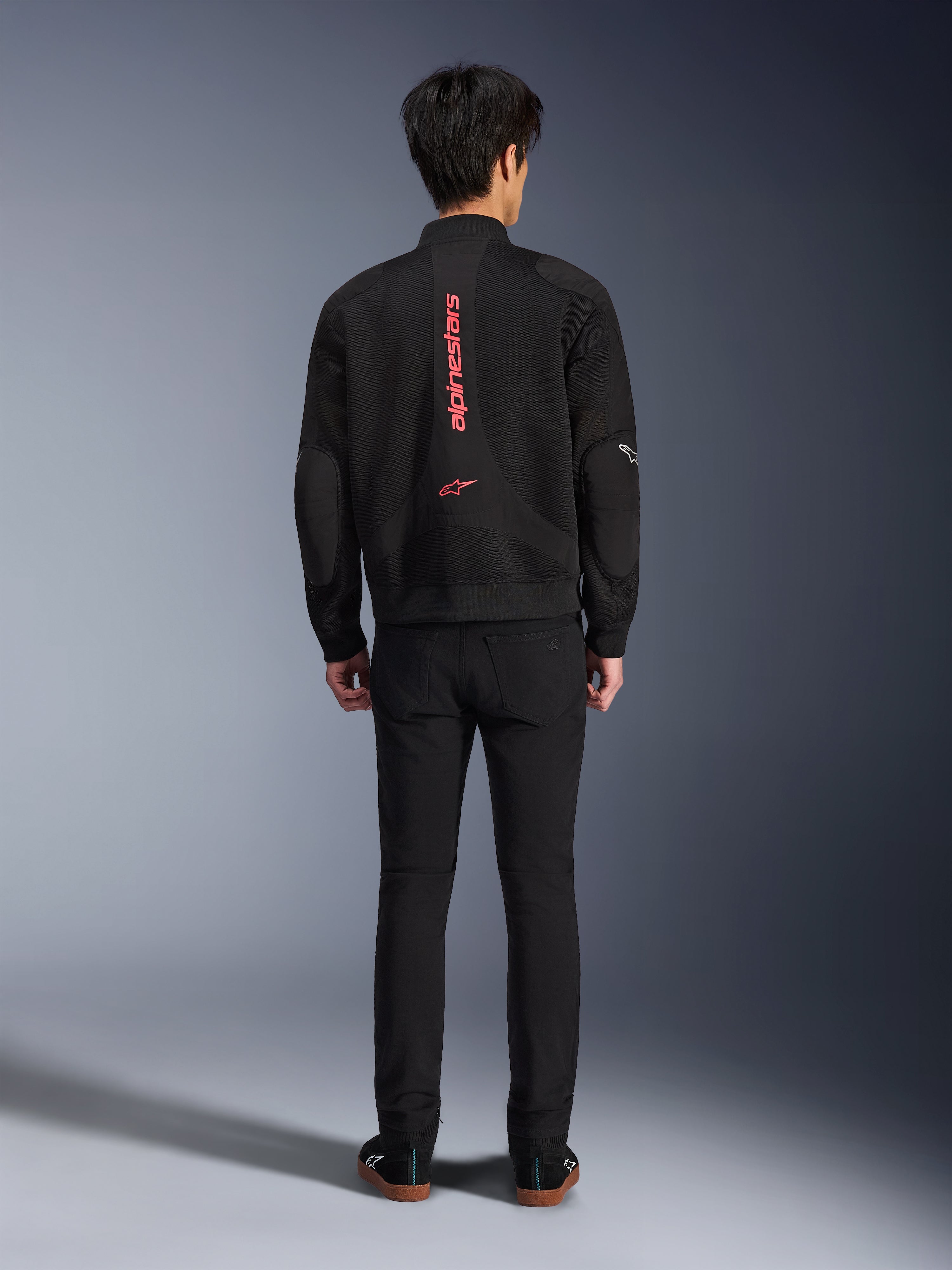 Giacca Alpinestars Flight Air in Nero Rosso Brillante, vista posteriore di giacca da moto in stile bomber urbano, con branding Alpinestars verticale rosso e logo sulla schiena, costruzione leggera in mesh 3D, indossata con pantaloni neri per un look contemporaneo.