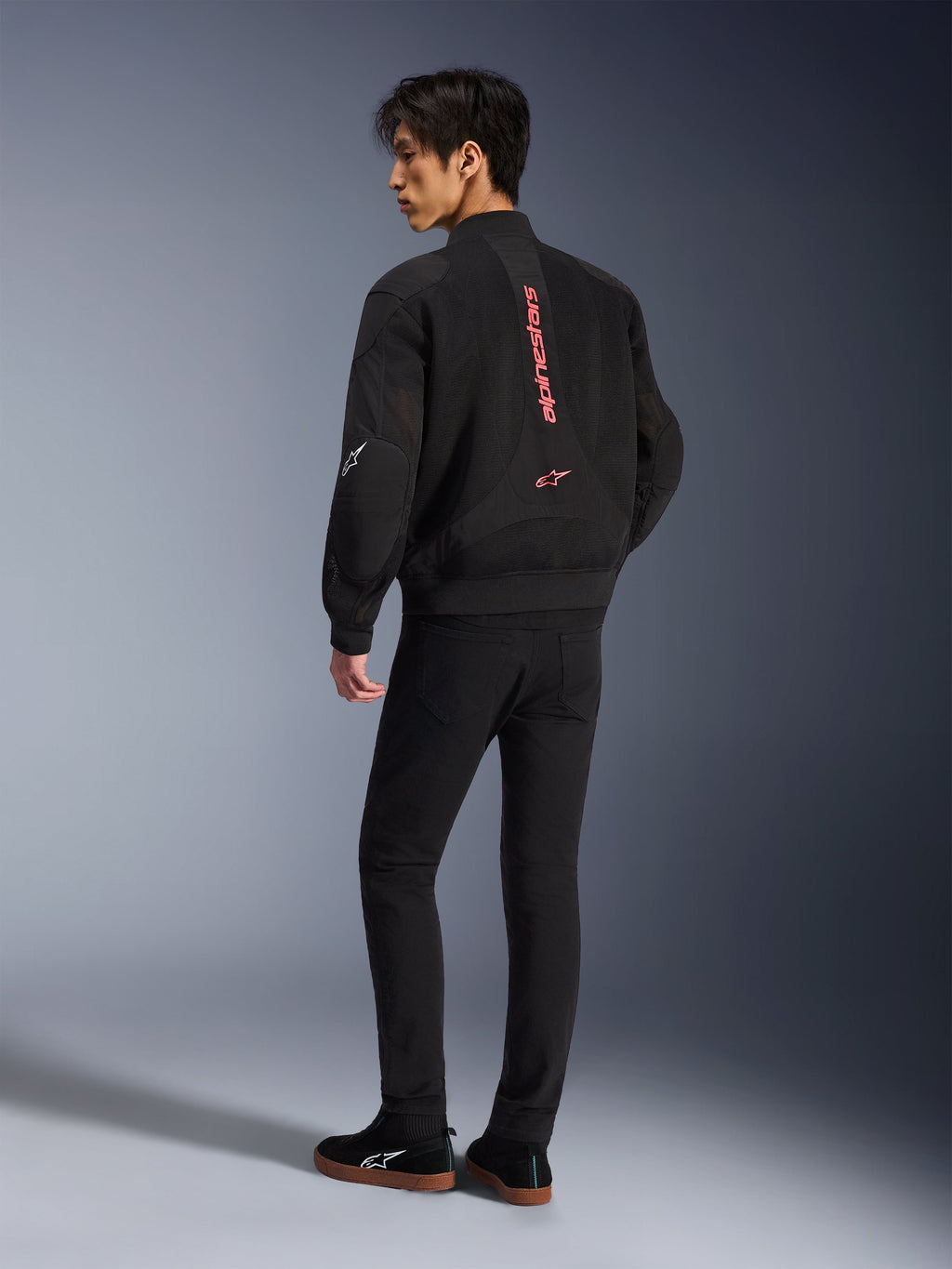 Modello con giacca Alpinestars Flight Air in Black Bright Red, vista posteriore che mostra il marchio rosso verticale sulla schiena e la costruzione in mesh 3D, abbinata a pantaloni neri e sneakers, stile motociclistico urbano