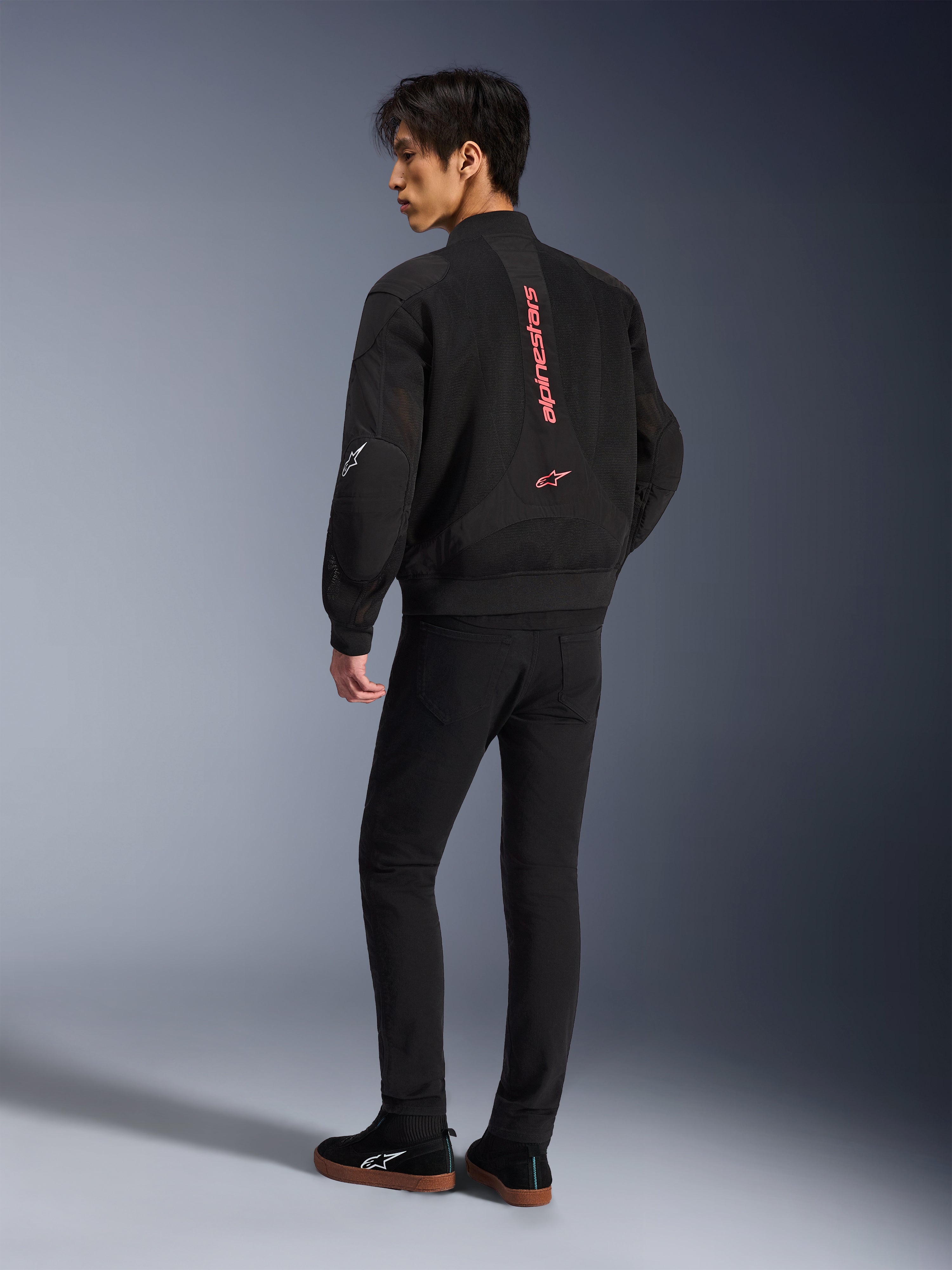 Modello con giacca Alpinestars Flight Air in Black Bright Red, vista posteriore che mostra il marchio rosso verticale sulla schiena e la costruzione in mesh 3D, abbinata a pantaloni neri e sneakers, stile motociclistico urbano