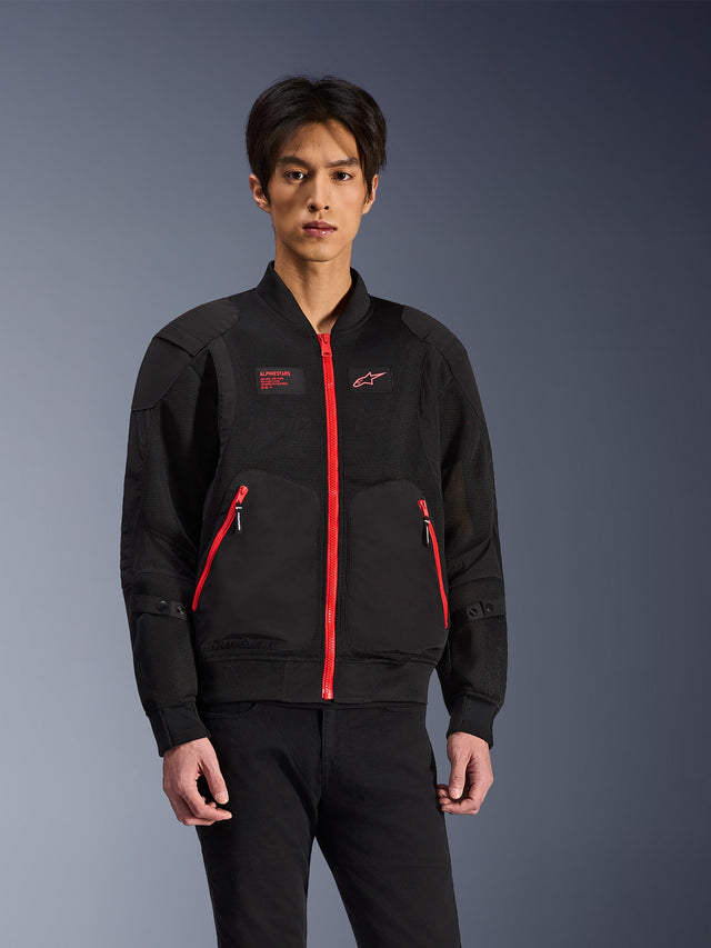 Alpinestars Flight Air Jacket in nero e rosso brillante, giacca da moto urbana in stile bomber indossata da un modello, con pannelli di ventilazione in mesh, una vistosa zip frontale rossa, dettagli delle tasche rossi e logo sul petto, abbinata a pantaloni neri
