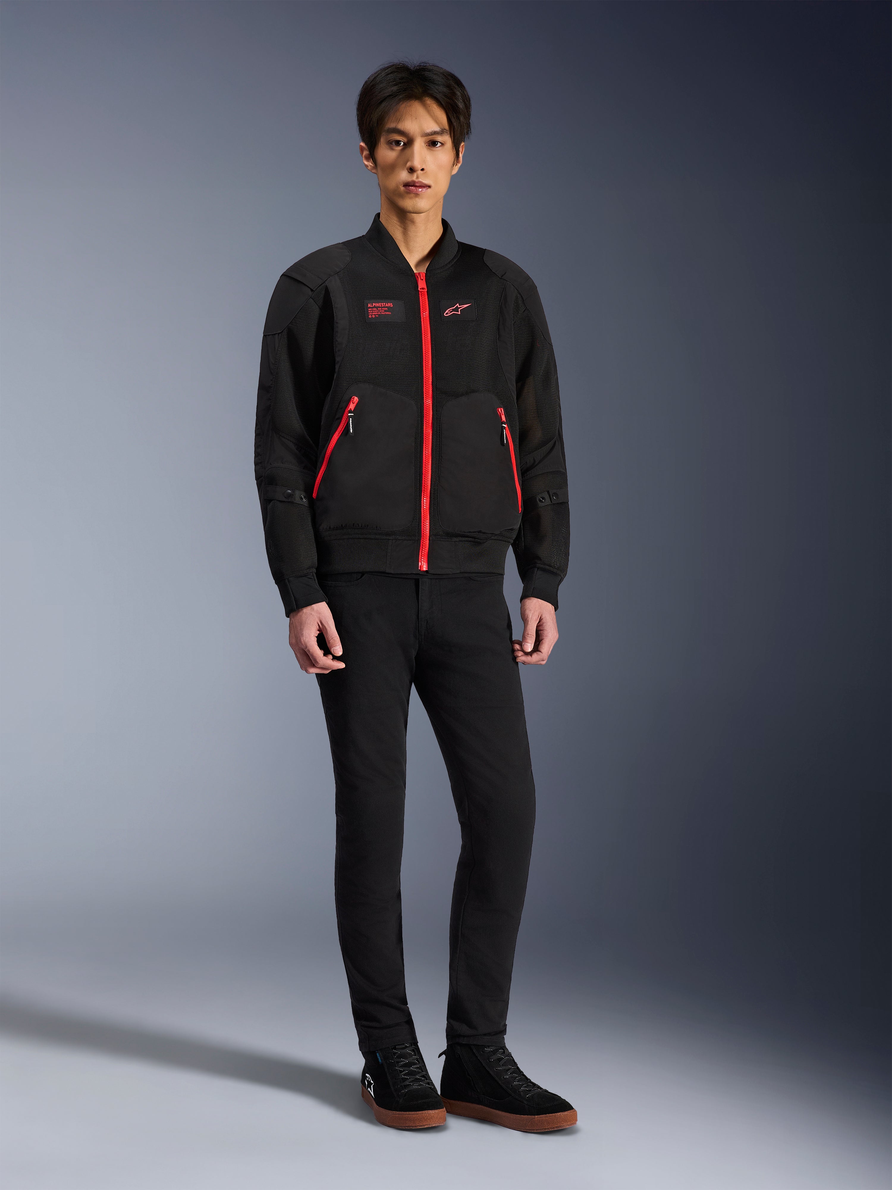 Giacca Alpinestars Flight Air in Nero e Rosso Brillante, giacca da moto urbana in stile bomber con pannelli in mesh 3D e vivaci cerniere rosse, indossata da un modello con pantaloni neri slim-fit e sneakers nere, abbigliamento da moto contemporaneo d'ispirazione street