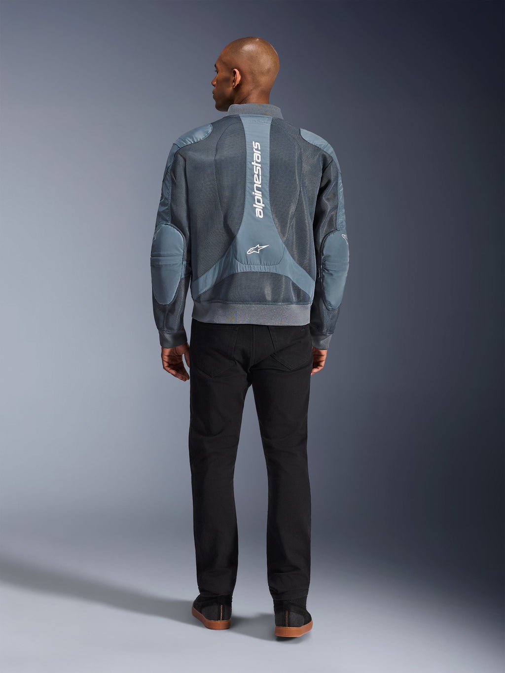 Giacca Alpinestars Flight Air in Storm Gray, vista posteriore di un modello che indossa una giacca da moto in stile urban con pannelli in mesh 3D e logo Alpinestars verticale, abbinata a pantaloni neri per un look da commuter moderno