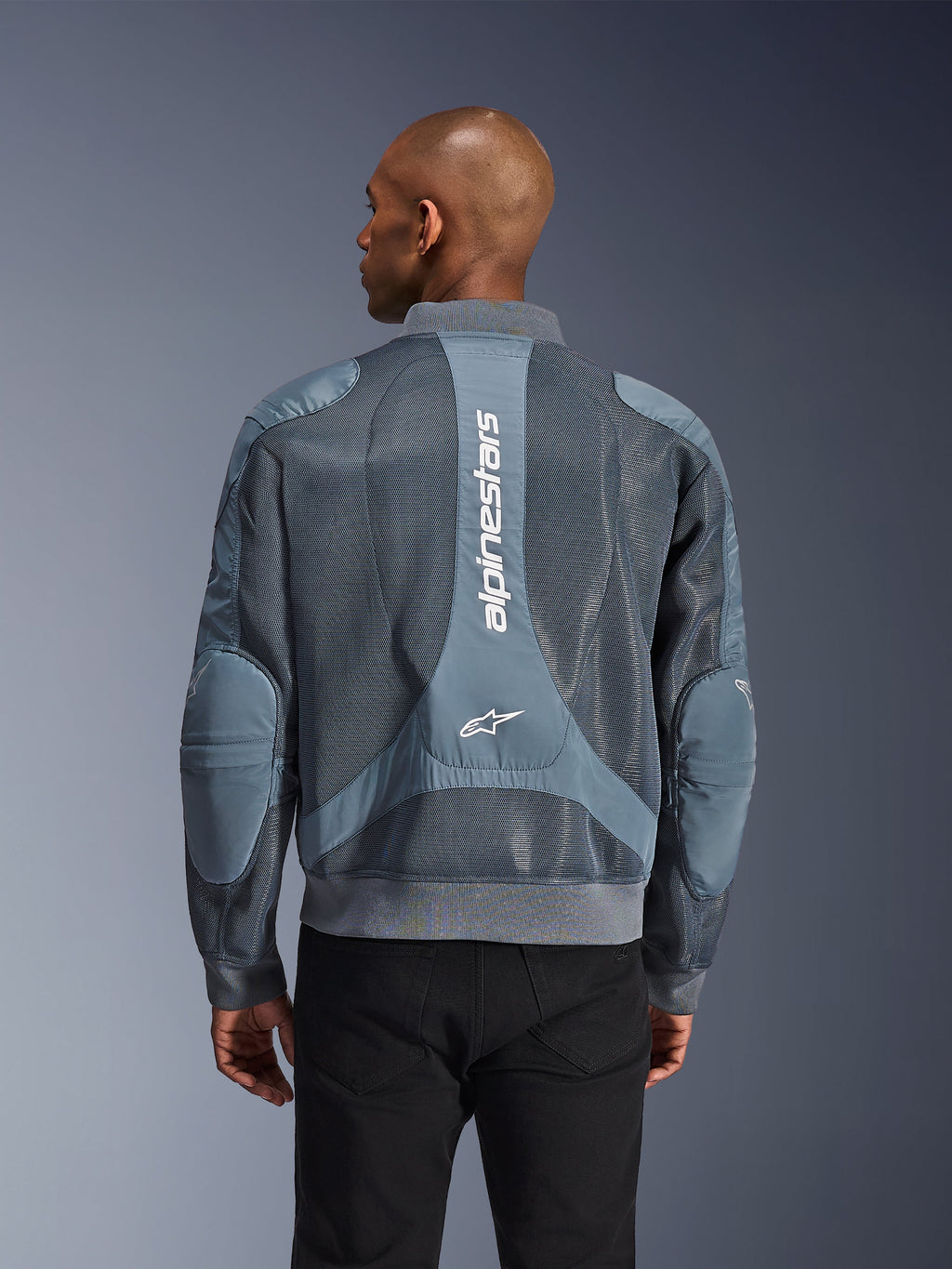 Giacca Alpinestars Flight Air in Storm Gray, vista posteriore su un modello, giacca da moto urbana con ampi pannelli in mesh 3D, marchio Alpinestars verticale sulla schiena e colletto e orlo a costine in stile bomber.