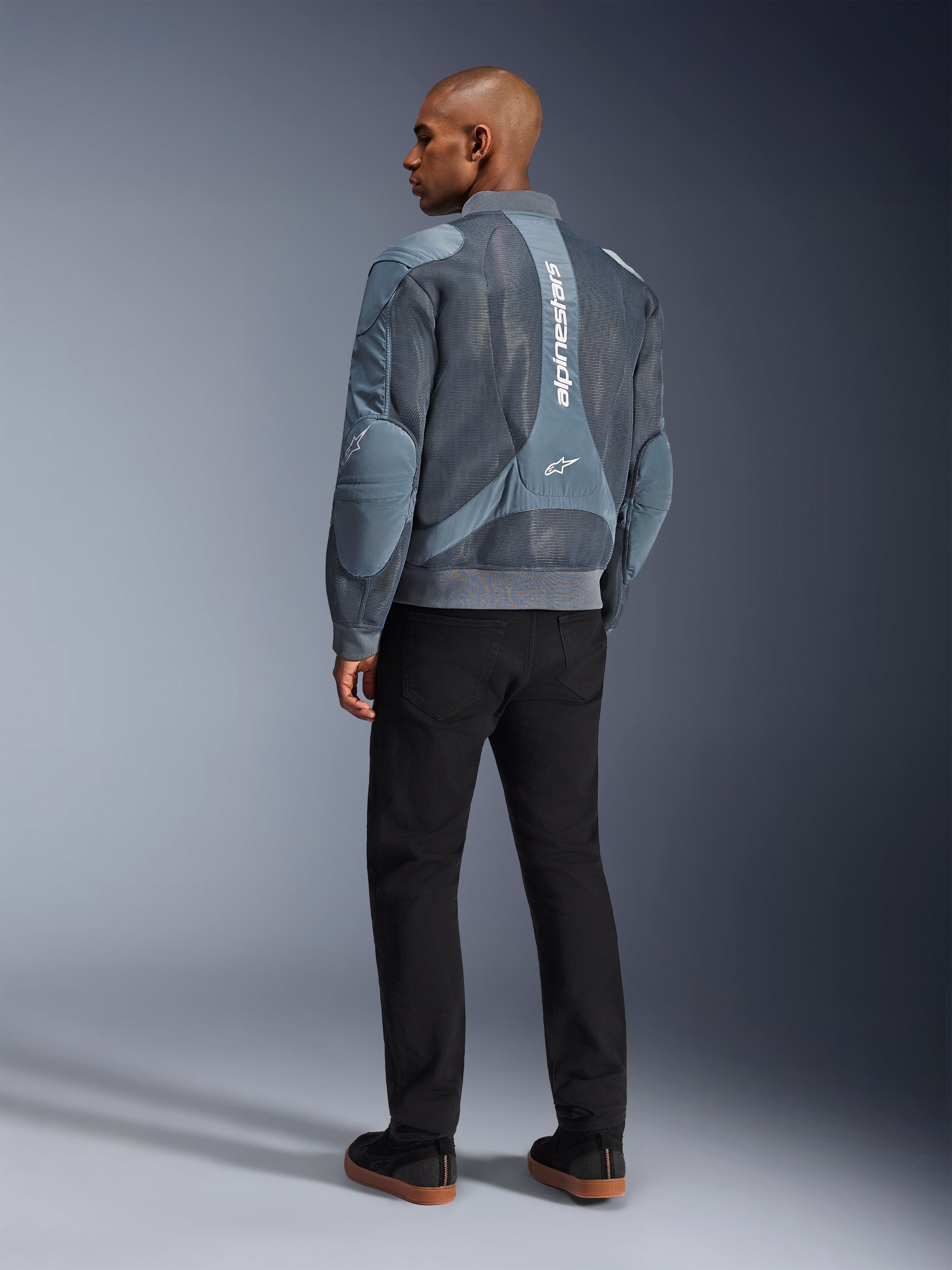 Alpinestars Flight Air Jacket, giacca da moto Storm Gray, vista posteriore, con pannelli di ventilazione in mesh 3D e marchio Alpinestars bianco verticale, indossata con pantaloni neri e sneakers nere, stile urban commuter