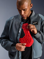 Giacca Alpinestars Flight Air in Storm Gray, giacca bomber da moto urbana con pannelli in mesh 3D per la ventilazione, aperta per mostrare un inserto paraschiena Nucleon rosso, con marchio 'Alpinestars Protects' ed estetica streetwear moderna