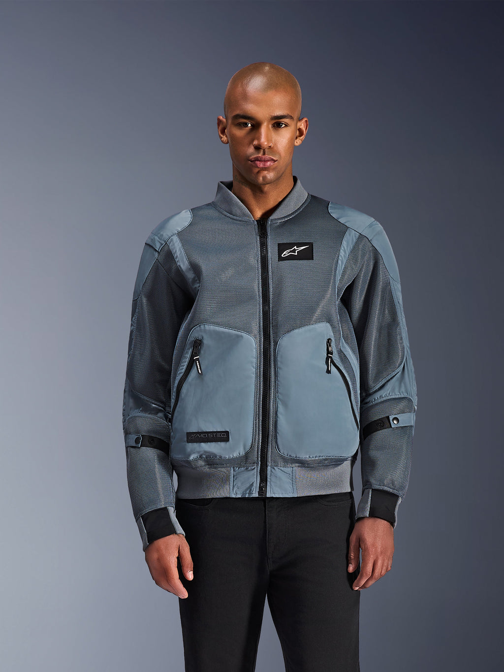 Giacca Alpinestars Flight Air, giacca da moto urban stile bomber, colore Storm Gray, dotata di pannelli di ventilazione in mesh 3D e patch con logo Astars bianco, indossata da un modello con pantaloni neri, abbigliamento da moto urbano contemporaneo