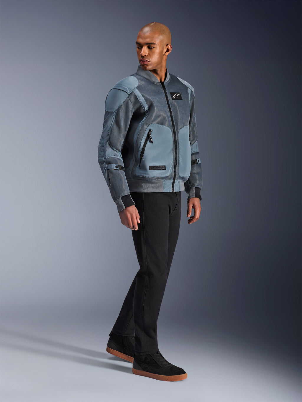 Giacca Alpinestars Flight Air, Storm Gray, giacca da moto in stile bomber urbano, indossata da un modello uomo con pantaloni neri e sneaker, con ampi pannelli di ventilazione in mesh 3D e tasche protettive esterne, abbigliamento streetwear tecnico per la guida in climi caldi