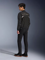Alpinestars Unite Jacket, giacca da moto urban, nero e grigio scuro, vista posteriore con grande logo Alpinestars profilato, profili e pannelli riflettenti, design softshell minimalista, indossata con pantaloni neri e calzature casual