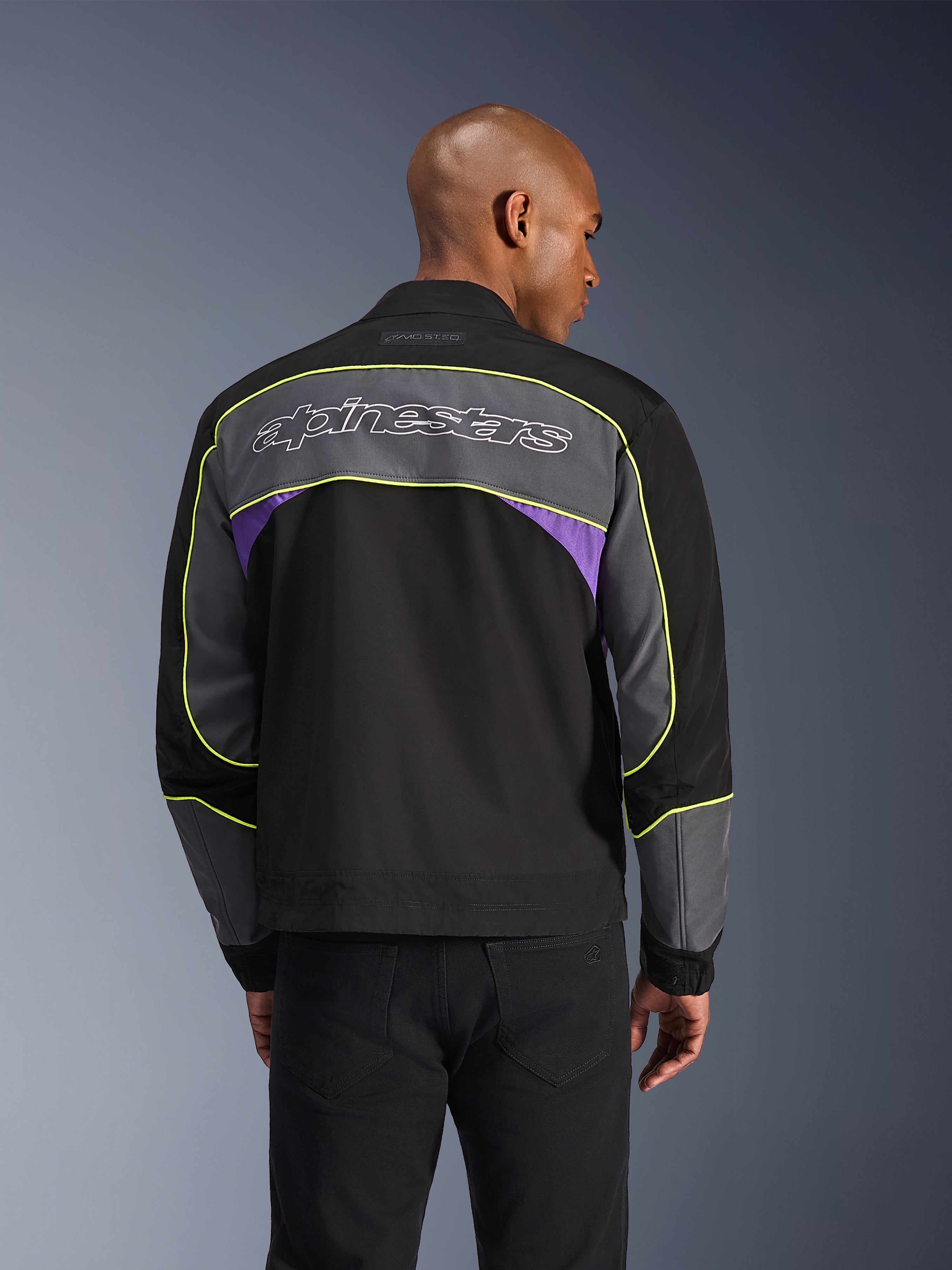 Alpinestars Giacca Unite, giacca da moto urbana, nero asphalt violet, vista posteriore con pannelli grigi e accenti viola, profili giallo lime, grande scritta Alpinestars sulla parte superiore della schiena, design streetwear minimalista
