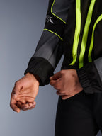 Giacca Alpinestars Unite, giacca da moto urbana, nero e asfalto con accenti giallo neon, primo piano delle mani che regolano il polsino elasticizzato della manica, abbigliamento protettivo minimalista ispirato allo streetwear