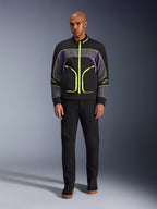 Modello che indossa la giacca Alpinestars Unite in Black Asphalt Violet, caratterizzata da una base nera con pannelli grigi e viola e vivaci cerniere e finiture giallo neon, abbinata a pantaloni e scarpe neri, giacca da moto urbana minimalista.