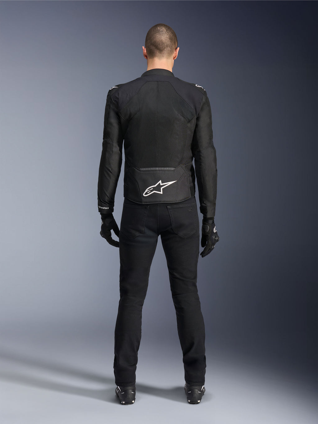 Giacca Alpinestars Viper Air V4, giacca da moto in tessuto nero, vista posteriore con logo a stella Alpinestars bianco sulla parte inferiore della schiena, indossata con pantaloni e guanti neri, abbigliamento estivo per guida stradale e sportiva