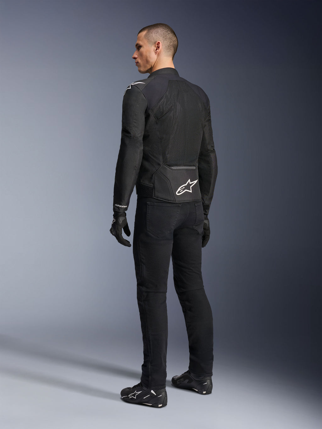 Giacca Alpinestars Viper Air V4, giacca da moto in tessuto nero, vista posteriore su un modello, con ampi pannelli in rete tecnica per la ventilazione e logo a stella bianco sulla parte bassa della schiena, indossata con pantaloni e guanti neri abbinati