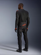 Pilota uomo visto da dietro che indossa la giacca Alpinestars Viper Air V4, nero e rosso fluo, con logo Astars arancione sulla parte bassa della schiena e sulle spalle, costruzione in tessuto mesh, abbinata a pantaloni e stivali da moto neri coordinati.