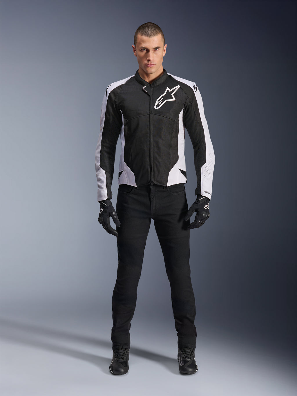 Giacca Alpinestars Viper Air V4, giacca da moto nera e bianca con grande logo bianco sul petto, indossata da un modello con pantaloni e guanti neri, con pannelli in mesh per la ventilazione, abbigliamento sportivo per guida su strada