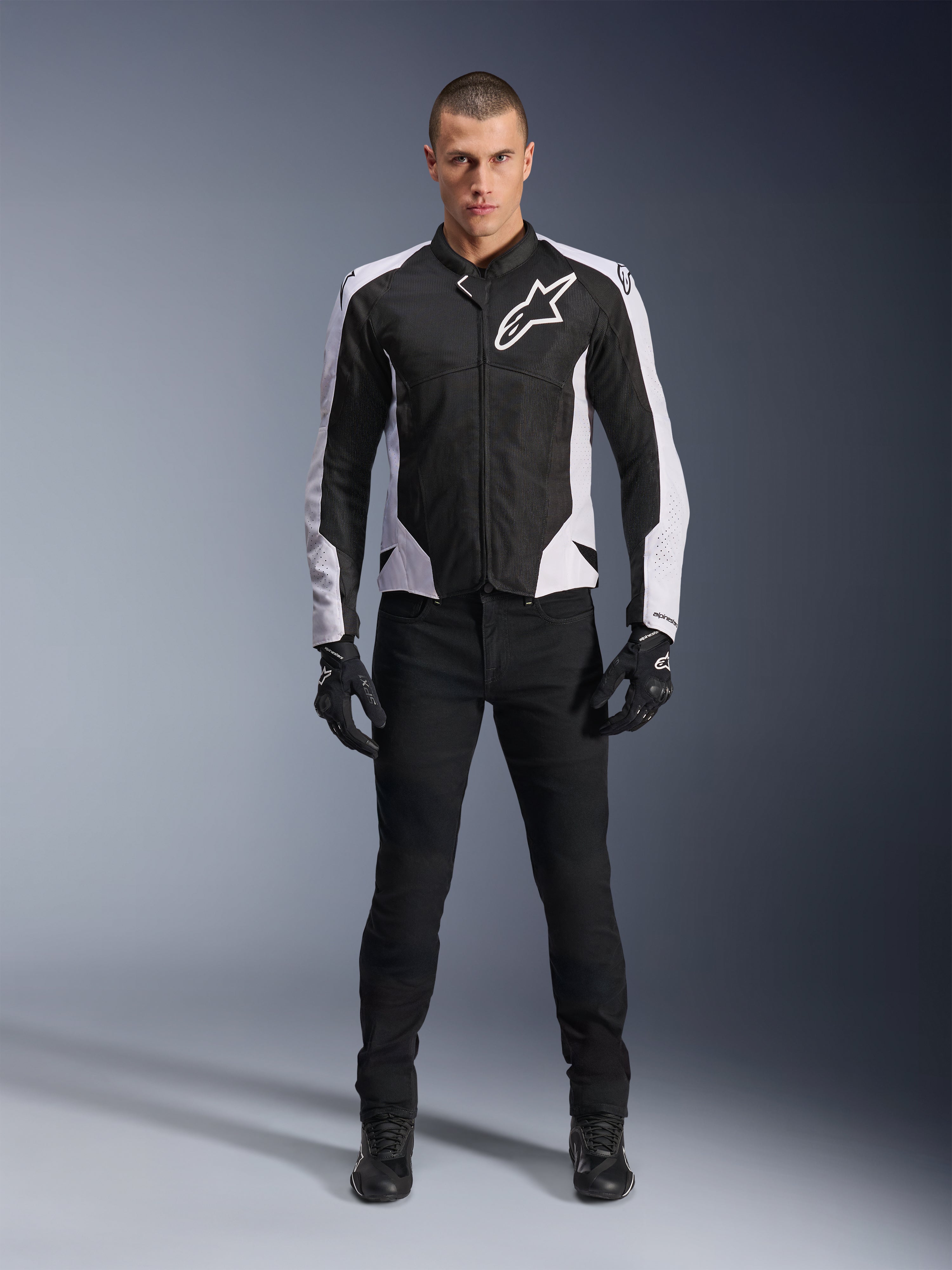 Giacca Alpinestars Viper Air V4, giacca da moto nera e bianca con grande logo bianco sul petto, indossata da un modello con pantaloni e guanti neri, con pannelli in mesh per la ventilazione, abbigliamento sportivo per guida su strada