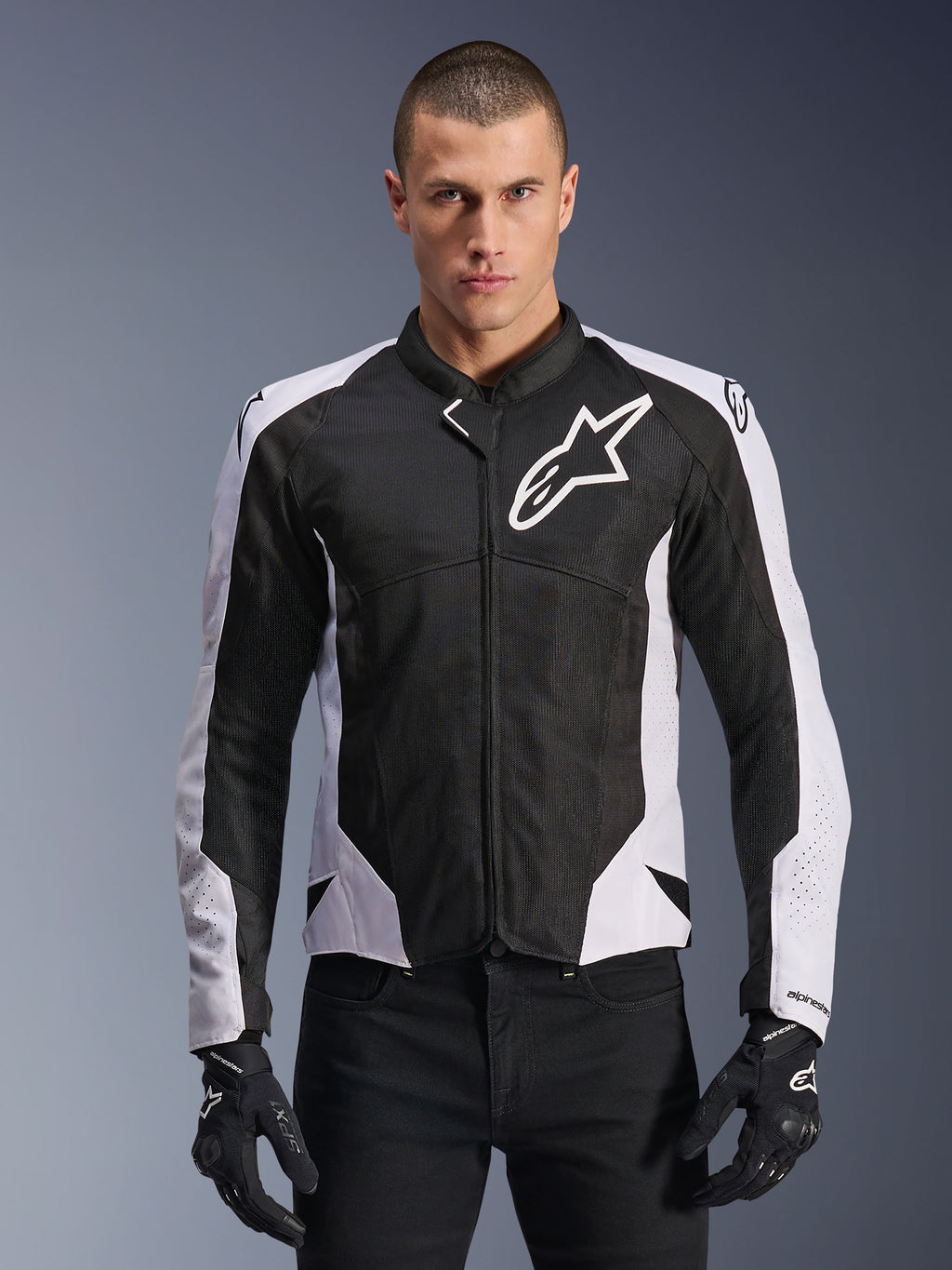 Alpinestars Viper Air V4 Jacket, giacca da moto racing, nero e bianco, indossata da un pilota, costruzione in mesh tecnico e tessuto con pannelli bianchi sulle spalle, logo a stella prominente sul petto, design sportivo, abbinata a guanti da moto neri