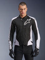 Alpinestars Viper Air V4 Jacket, giacca da moto racing, nero e bianco, indossata da un pilota, costruzione in mesh tecnico e tessuto con pannelli bianchi sulle spalle, logo a stella prominente sul petto, design sportivo, abbinata a guanti da moto neri