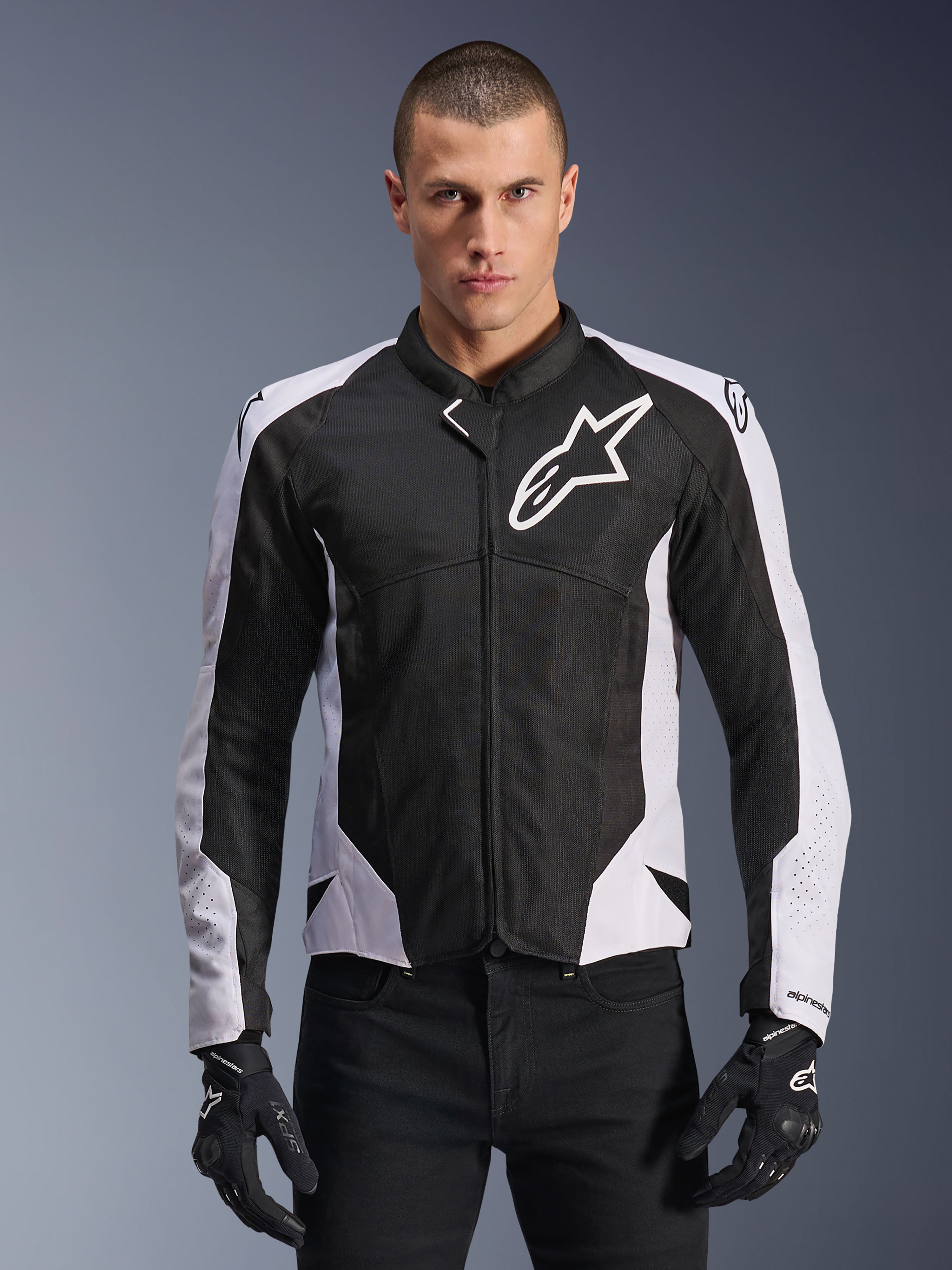 Alpinestars Viper Air V4 Jacket, giacca da moto racing, nero e bianco, indossata da un pilota, costruzione in mesh tecnico e tessuto con pannelli bianchi sulle spalle, logo a stella prominente sul petto, design sportivo, abbinata a guanti da moto neri
