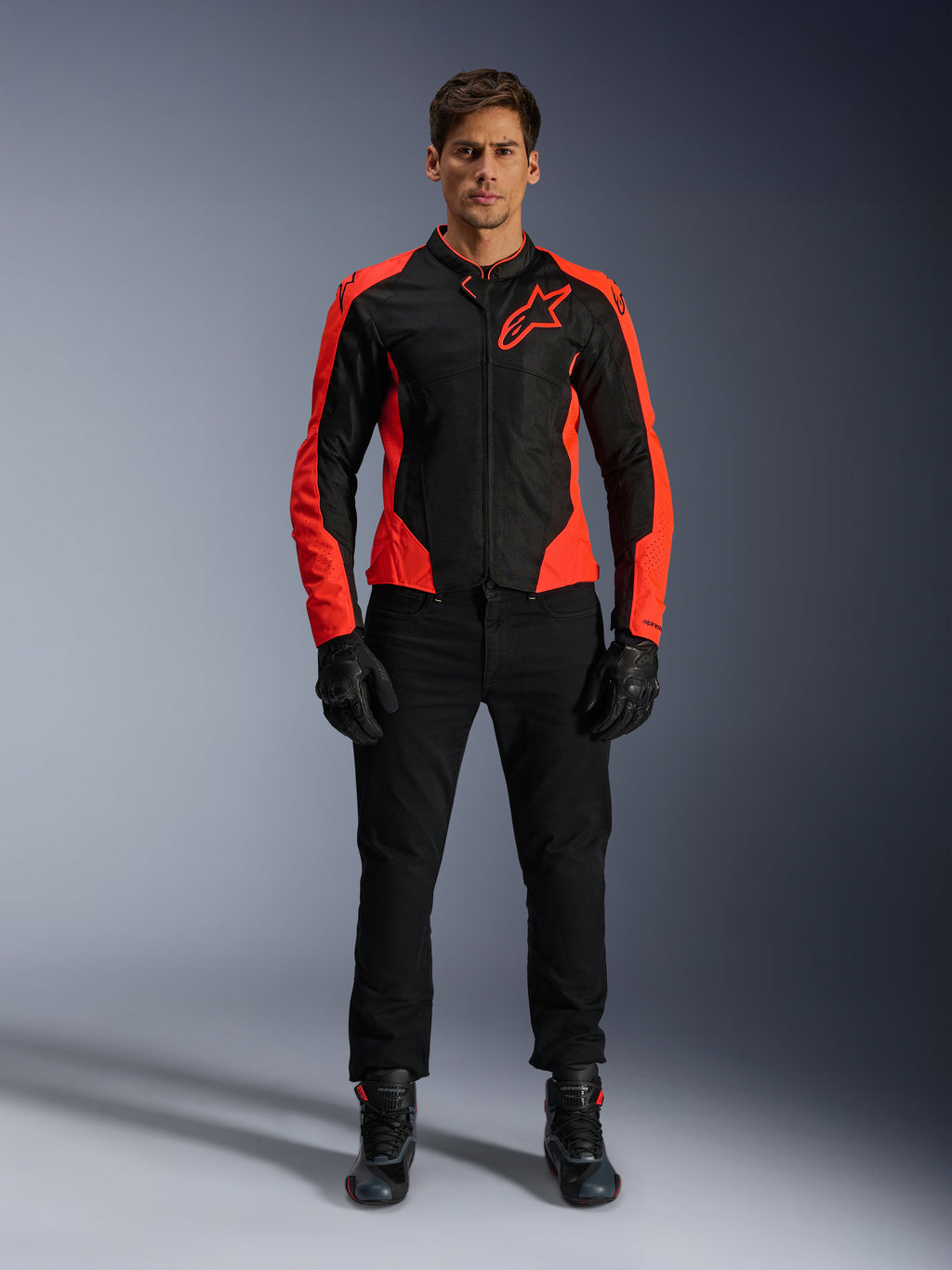 Modello che indossa la giacca Alpinestars Viper Air V4 in rosso fluo e nero, abbinata a pantaloni da moto, guanti e stivali neri, con pannelli in mesh traspirante per la ventilazione e un audace logo a stella sul petto, abbigliamento sportivo da moto da strada