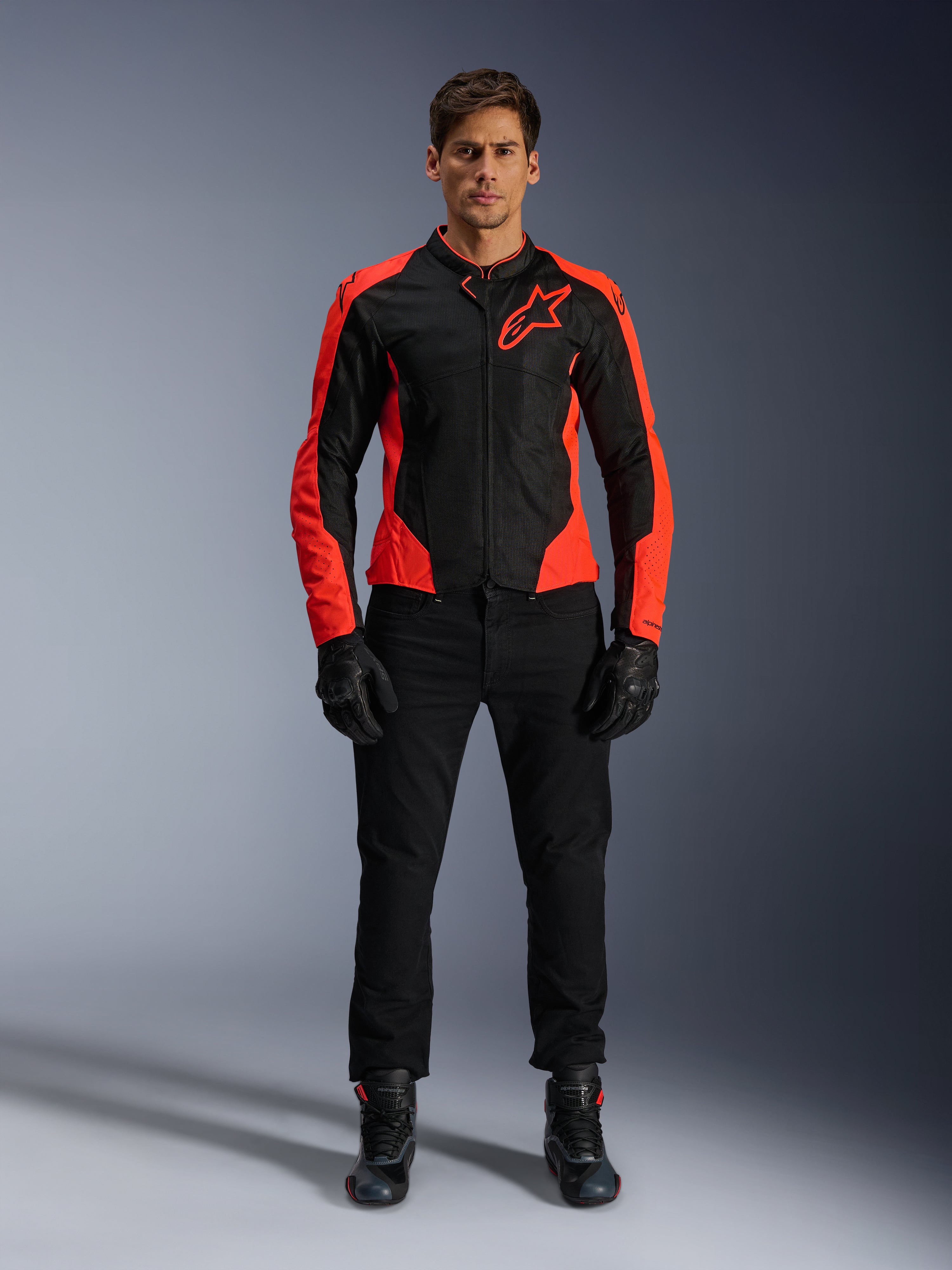 Modello che indossa la giacca Alpinestars Viper Air V4 in rosso fluo e nero, abbinata a pantaloni da moto, guanti e stivali neri, con pannelli in mesh traspirante per la ventilazione e un audace logo a stella sul petto, abbigliamento sportivo da moto da strada