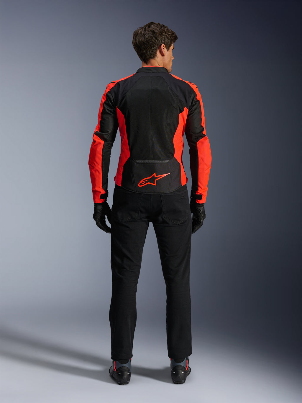 Giacca Alpinestars Viper Air V4, rosso fluo e nero, vista posteriore con ampi pannelli in mesh tecnico e accenti laterali in rosso fluorescente, logo Alpinestars rosso sulla parte bassa della schiena, indossata con pantaloni da guida e guanti neri.