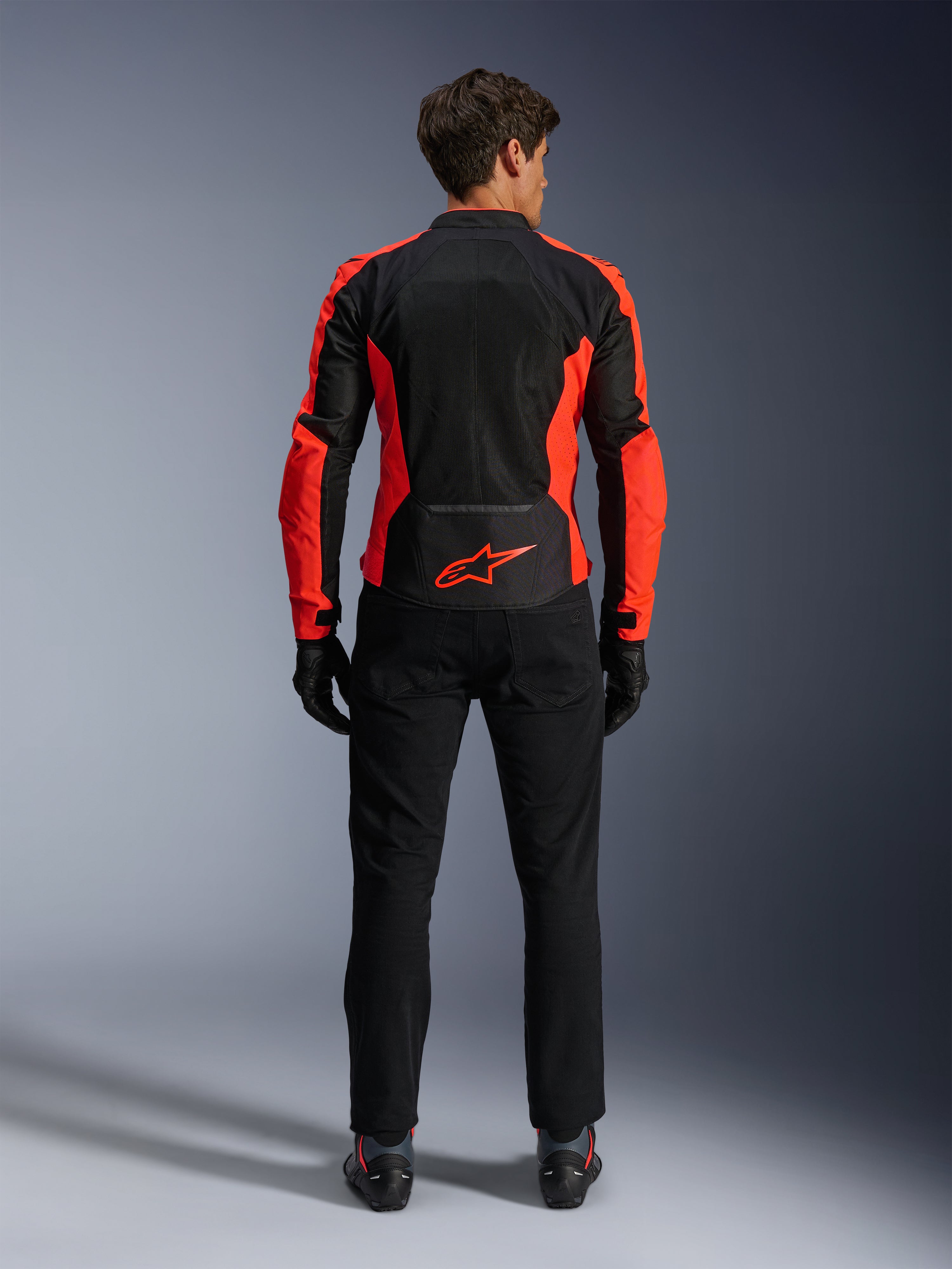 Giacca Alpinestars Viper Air V4, rosso fluo e nero, vista posteriore con ampi pannelli in mesh tecnico e accenti laterali in rosso fluorescente, logo Alpinestars rosso sulla parte bassa della schiena, indossata con pantaloni da guida e guanti neri.