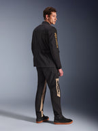 Giacca Alpinestars Dice, giacca da moto urbana, nero, vista posteriore a 3/4 su modello, caratterizzata da un'estetica vintage field jacket con logo Alpinestars dorato sulla manica, indossata con pantaloni da moto coordinati nero e beige e sneakers nere