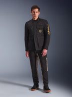 Modello che indossa la giacca Alpinestars Dice Jacket, giacca da moto urbana nera con stile vintage da field jacket, quattro tasche anteriori funzionali, logo Alpinestars sulla manica e sul petto, abbinata a pantaloni neri e beige, abbigliamento moderno per la guida urbana