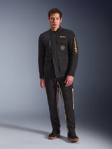 Modello che indossa la giacca Alpinestars Dice Jacket, giacca da moto urbana nera con stile vintage da field jacket, quattro tasche anteriori funzionali, logo Alpinestars sulla manica e sul petto, abbinata a pantaloni neri e beige, abbigliamento moderno per la guida urbana