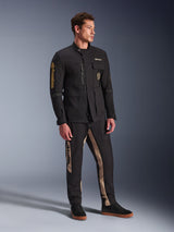 Modello che indossa la giacca Alpinestars Dice Jacket in nero, giacca da moto urbana dall'estetica vintage field jacket, con tasche utility multiple e logo dorato sulla manica, abbinata a pantaloni coordinati neri e tan e sneaker nere.