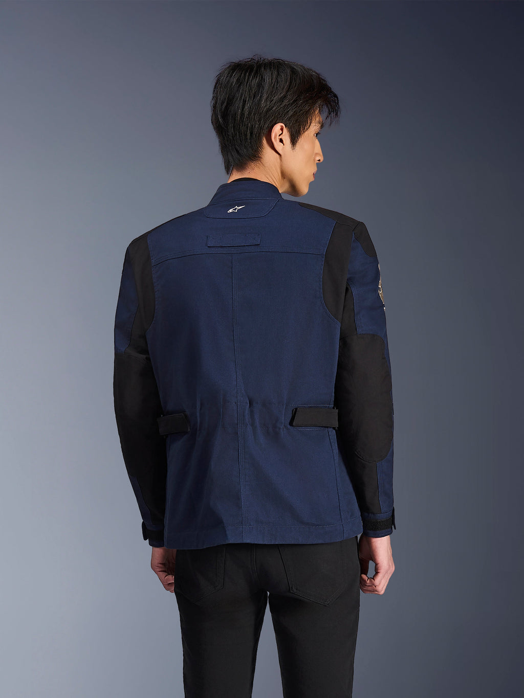 Alpinestars Dice Jacket, giacca da moto urbana stile field blu scuro e nera, vista posteriore indossata da un uomo, con pannelli neri rinforzati su spalle e gomiti e linguette di regolazione in vita.