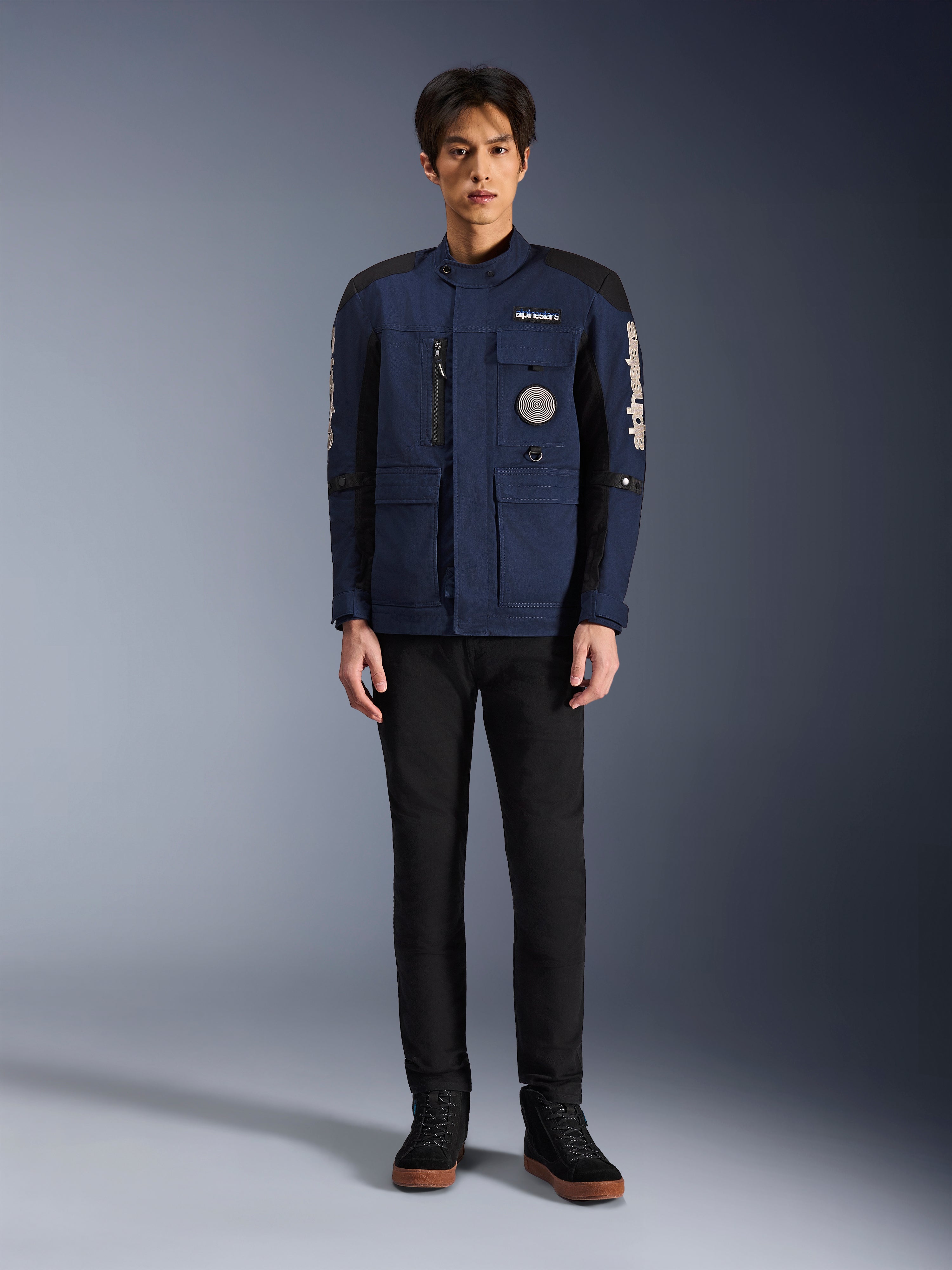 Alpinestars Dice Jacket, giacca da moto urban, blu scuro e nero, indossata da un modello con pantaloni neri e scarpe nere, design moderno da giacca da campo con tasche multiple, cerniera verticale sul petto e marchio Alpinestars bianco sulle maniche.