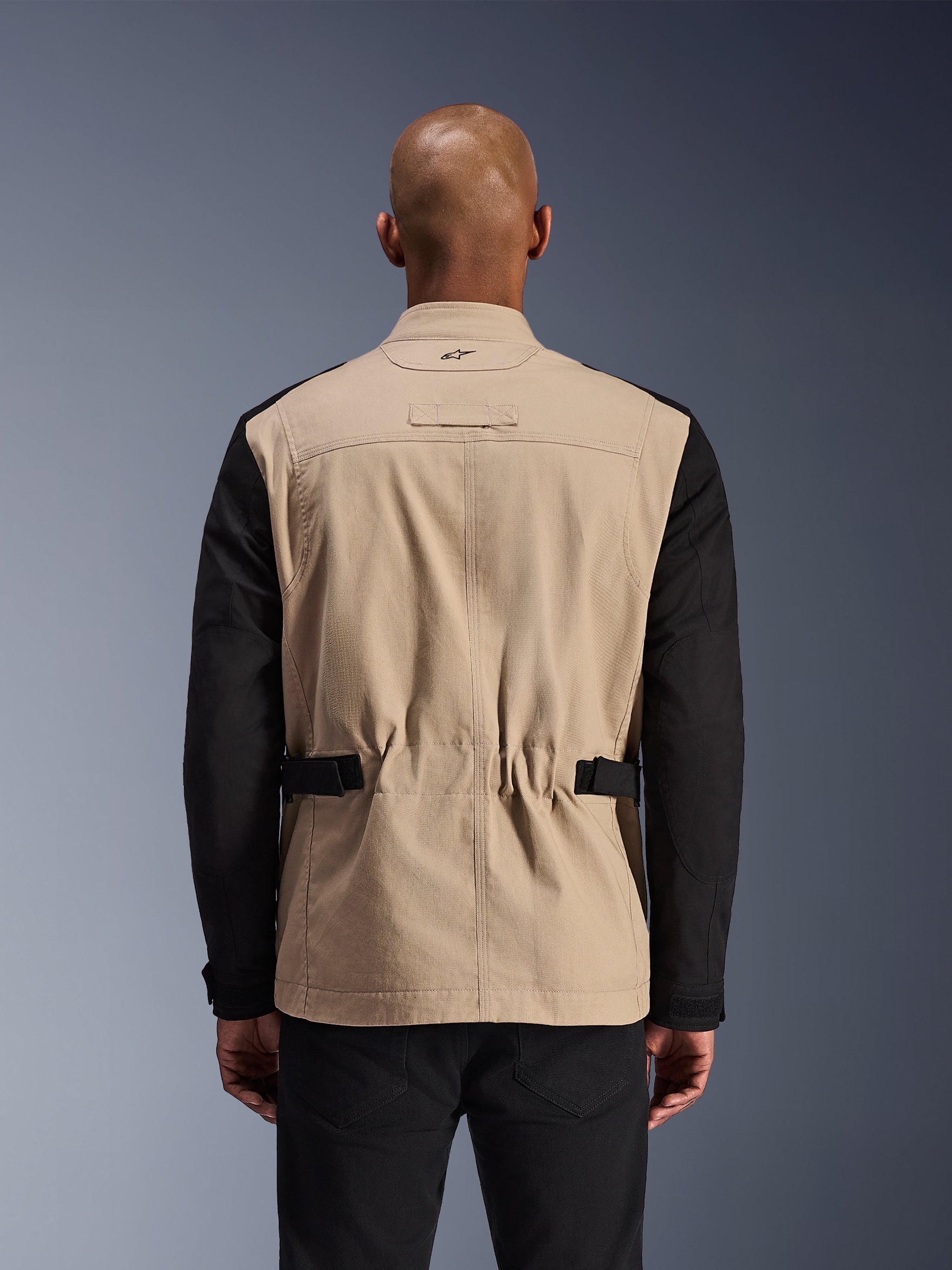Alpinestars Dice Jacket, giacca da moto urbana, alluminio e nero, vista posteriore su un modello, con spalle plissettate per la mobilità, cinturini regolabili in vita e una robusta costruzione in twill di policotone.