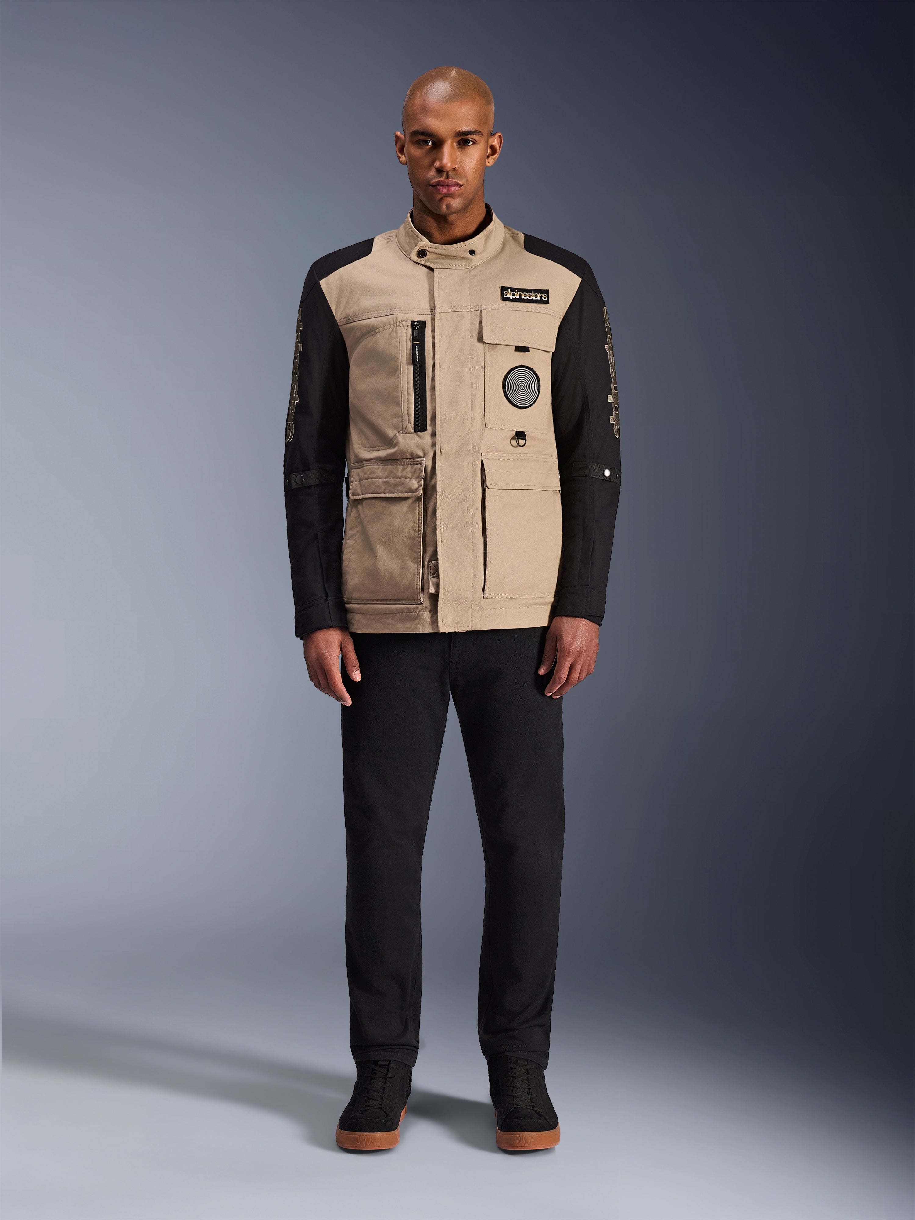 Giacca Alpinestars Dice, giacca da moto urbana, corpo color alluminio con maniche nere, silhouette ispirata al workwear con quattro tasche utility frontali, indossata con pantaloni neri e sneaker alte nere, abbigliamento tecnico da moto robusto in stile urban