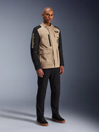 Alpinestars Giacca Dice, giacca da moto urbana, Aluminum Black e tan, design bicolore con maniche nere e busto khaki, indossata da un modello con pantaloni neri e sneakers nere, estetica ispirata al workwear con tasche utility e marchio ricamato sulla manica.