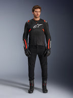 Modello che indossa la giacca Alpinestars T-SPS Air v2, giacca da moto in tessuto nero con dettagli rosso fluo, logo bianco sul petto, abbinata a pantaloni, guanti e stivali neri, stile di guida urban sport