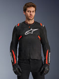 Alpinestars Giacca T-Sps Air V2, giacca da moto nero e rosso fluo, grande logo Astars bianco sul petto, costruzione in rete tecnica per una ventilazione ottimale, indossata da un modello con guanti da moto neri, design dal taglio sportivo con accenti rossi su spalle e maniche
