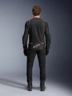Giacca Alpinestars T-SPS Air v2 in Nero e Rosso Fluo, vista posteriore che mostra ampi pannelli di ventilazione in rete e il logo Alpinestars bianco sulla parte bassa della schiena, indossata con pantaloni da guida e stivali neri.
