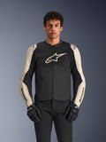 Alpinestars T-SPS Air V2 Jacket, giacca da moto, nero e mastic aluminum, modello maschile che indossa la giacca con pantaloni neri e guanti, con pannelli in rete per la ventilazione, grande logo Alpinestars sul petto e design sportivo aderente