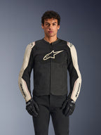 Alpinestars T-SPS Air V2 Jacket, giacca da moto, nero e mastic aluminum, modello maschile che indossa la giacca con pantaloni neri e guanti, con pannelli in rete per la ventilazione, grande logo Alpinestars sul petto e design sportivo aderente