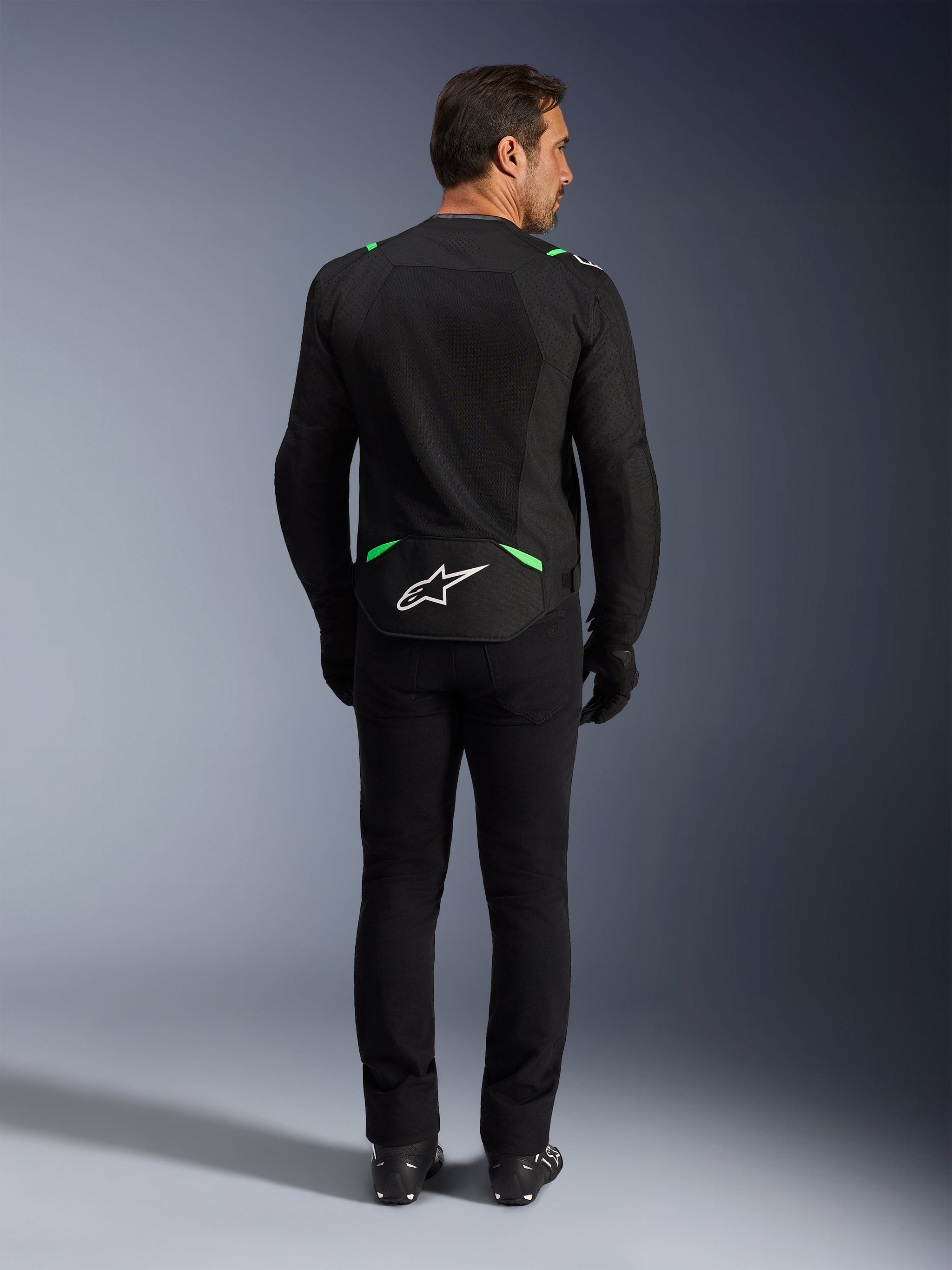 Giacca Alpinestars T-SPS Air V2, giacca da moto, nero e verde fluo, vista posteriore con logo bianco sulla parte bassa della schiena, indossata con pantaloni e stivali neri coordinati, design in rete ventilata per guida sportiva