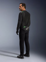 Giacca Alpinestars T-SPS Air V2 in Nero Verde Fluo indossata da un uomo, vista di profilo posteriore e laterale, abbinata a pantaloni da guida neri e scarpe da moto. La giacca presenta pannelli in rete tecnica ventilata, accenti verde fluo su spalle e parte bassa della schiena e il logo a stella bianco sul retro.