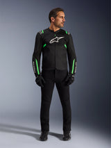 Uomo che indossa la giacca Alpinestars T-SPS Air V2 in nero e verde fluo, abbinata a pantaloni neri, guanti e scarpe da moto, caratterizzata da un design dal taglio sportivo con loghi bianchi e pannelli in rete per un look da guida urbana moderno.