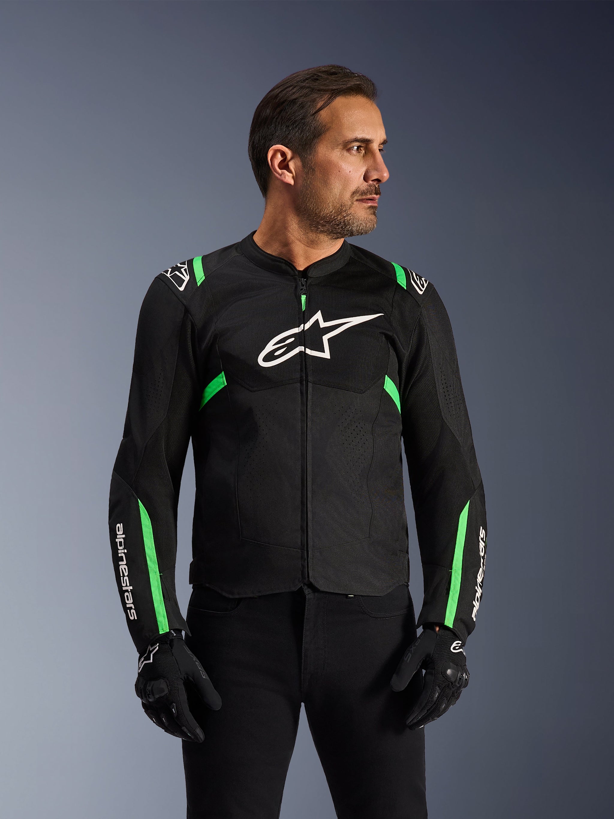 Giacca Alpinestars T-SPS Air V2, giacca da moto, nero e verde fluo, indossata da un modello con guanti e pantaloni neri, logo Alpinestars bianco sul petto e accenti verde neon su spalle e maniche, pannelli in rete tecnica per la ventilazione, design dal taglio sportivo per guida urbana