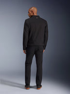 Giacca Alpinestars Bruiser in nero, vista posteriore di un modello che indossa la giacca da moto urbana con pantaloni neri coordinati, con un piccolo logo dorato sul colletto e regolatori in vita, estetica ispirata al workwear
