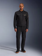 Giacca Alpinestars Bruiser, giacca da moto urbana nera, indossata da un modello con pantaloni neri e sneakers alte, vista frontale con tasche pettorali con cerniera e logo ricamato, design classico di ispirazione workwear per gli spostamenti quotidiani