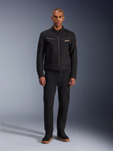 Giacca Alpinestars Bruiser, giacca da moto urbana nera, indossata da un modello con pantaloni neri e sneakers alte, vista frontale con tasche pettorali con cerniera e logo ricamato, design classico di ispirazione workwear per gli spostamenti quotidiani
